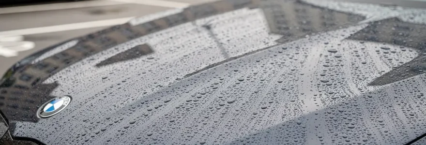 Gouttes d'eau perlant sur capot de berline sombre après pluie légère, effet hydrophobe coating céramique